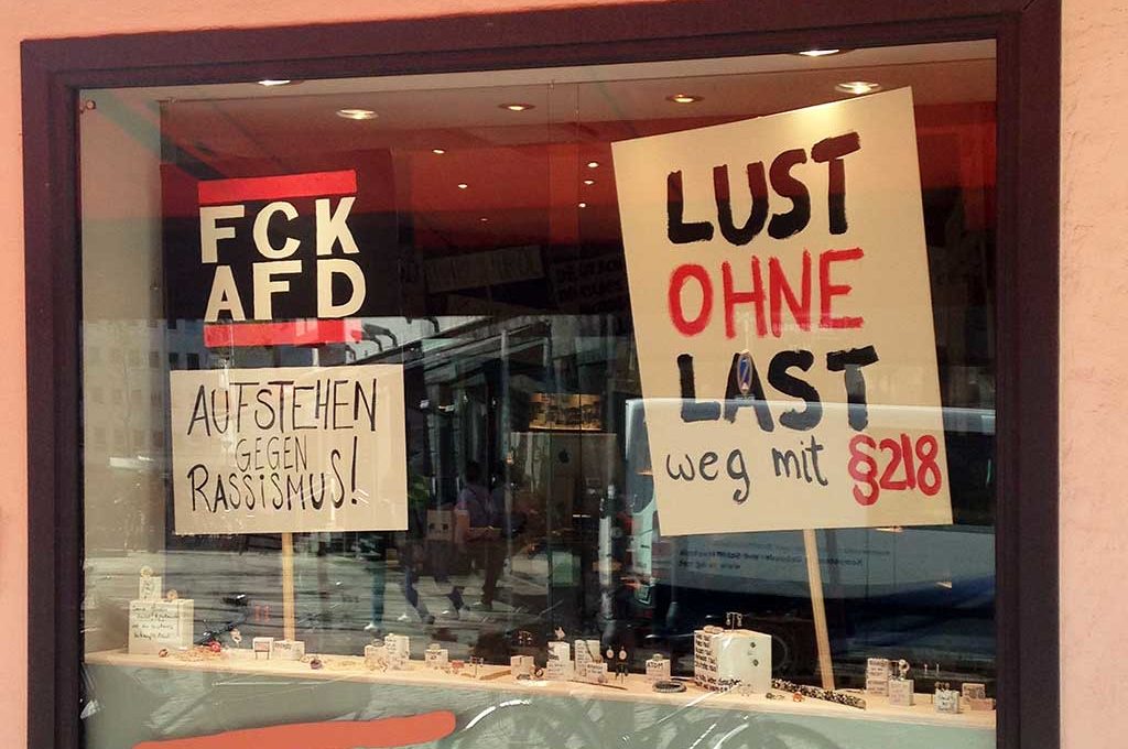 „Fuck AFD“ und „LUST OHNE LAST“-Schilder im Schaufenster