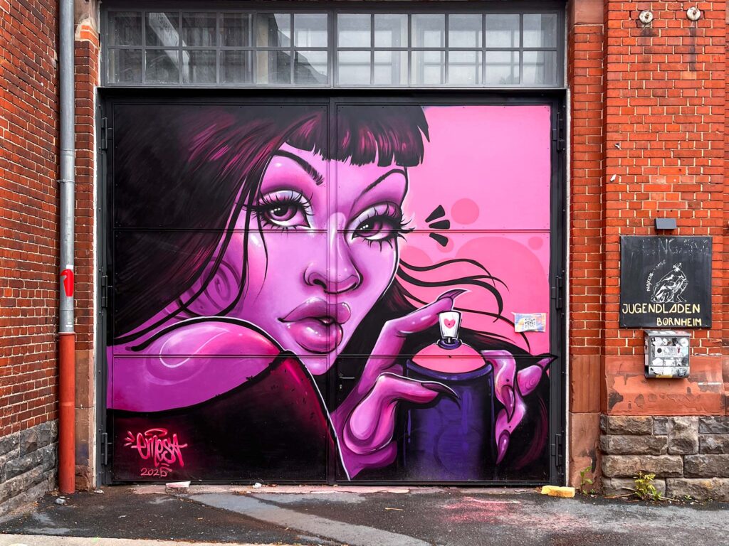 Bild einer Frau, die ganz in rosafarbenen Tönen gemalt ist, und eine Sprühdose hält. Gemalt von Urban-Art-Künstlerin Emesa an der Tür des Naxos Ateliers in Frankfurt am Main