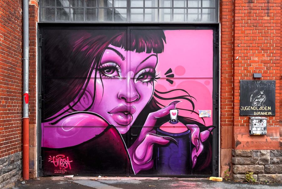 Bild einer Frau, die ganz in rosafarbenen Tönen gemalt ist, und eine Sprühdose hält. Gemalt von Urban-Art-Künstlerin Emesa an der Tür des Naxos Ateliers in Frankfurt am Main