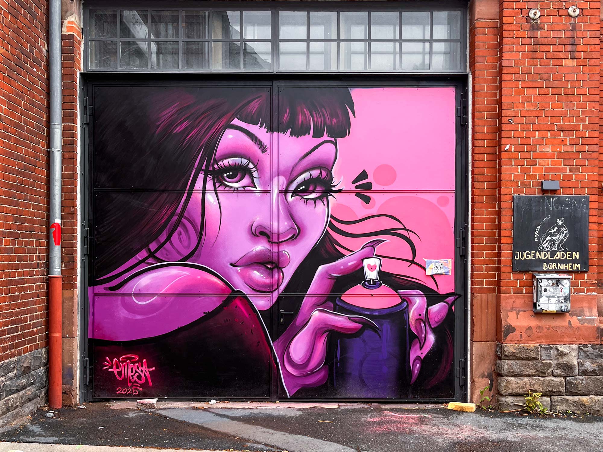 Bild einer Frau, die ganz in rosafarbenen Tönen gemalt ist, und eine Sprühdose hält. Gemalt von Urban-Art-Künstlerin Emesa an der Tür des Naxos Ateliers in Frankfurt am Main