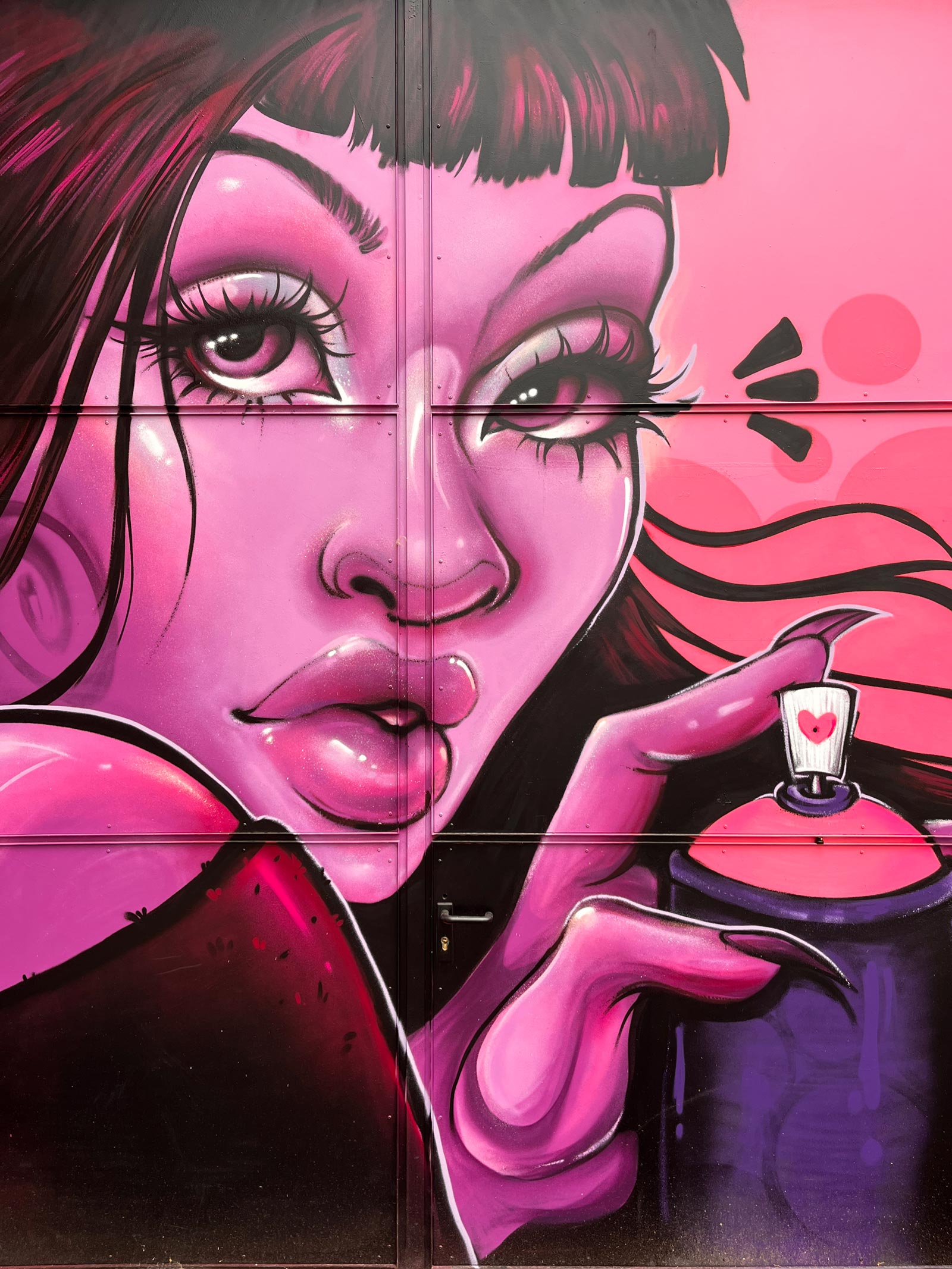 Bild einer Frau, die ganz in rosafarbenen Tönen gemalt ist, und eine Sprühdose hält. Gemalt von Urban-Art-Künstlerin Emesa an der Tür des Naxos Ateliers in Frankfurt am Main