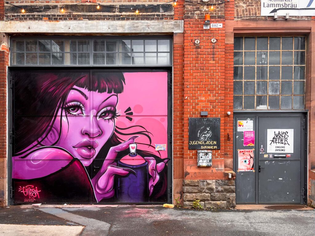 Bild einer Frau, die ganz in rosafarbenen Tönen gemalt ist, und eine Sprühdose hält. Gemalt von Urban-Art-Künstlerin Emesa an der Tür des Naxos Ateliers in Frankfurt am Main