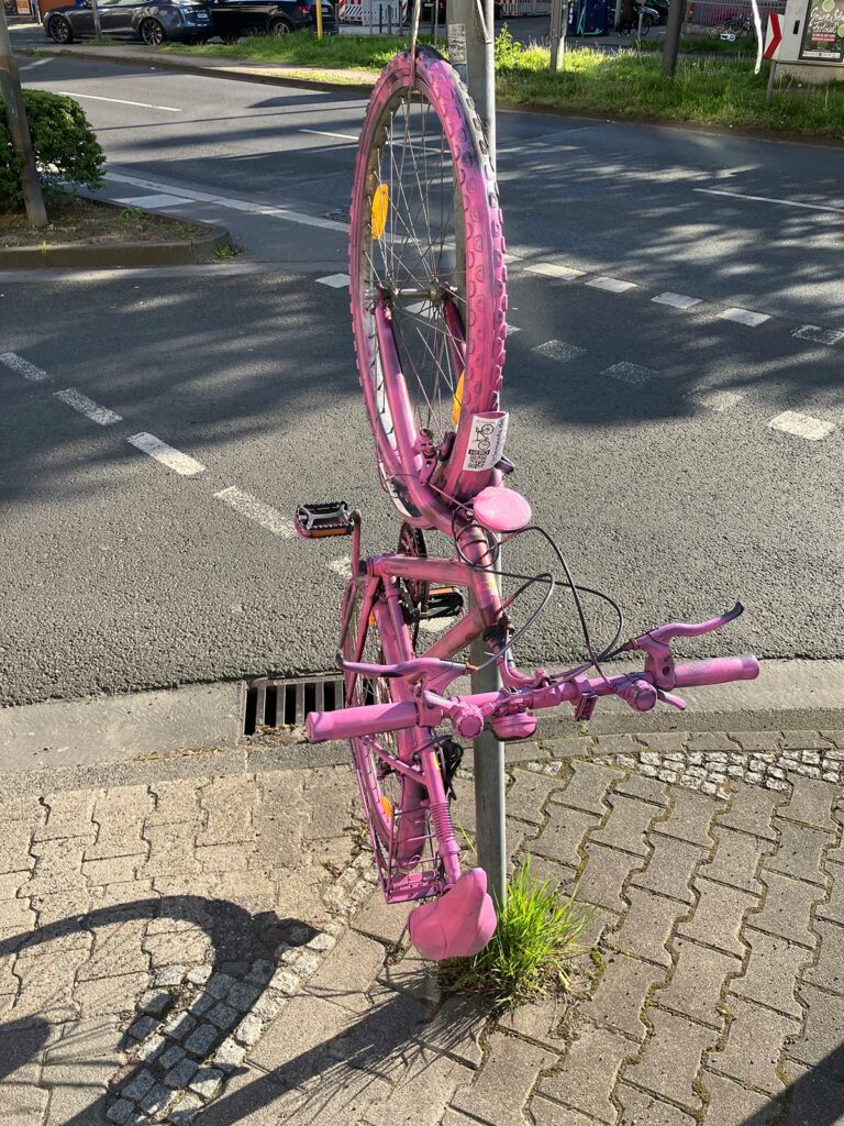 Fahrrad zuerst pink dann gold, hochkant befestigt an Verkehrsschild-Pfosten in Frankfurt