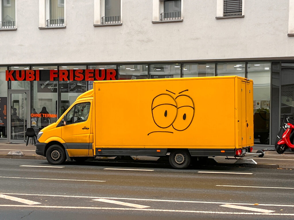 Gelber Transporter mit stilisiertem Gesicht mit großen Augen und nach unten gerichteten Augenbrauen und Mundlinien