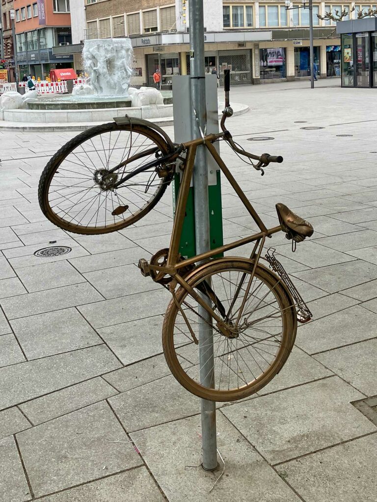 Goldenes Fahrrad hochkant befestigt an Straßenschuld-Stange in Frankfurt