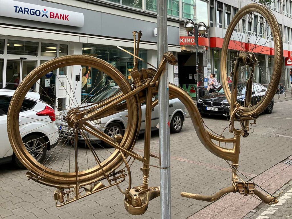 Goldenes Fahrrad hochkant befestigt an Verkehrsschild-Rohrpfosten in der Berger Straße in Frankfurt