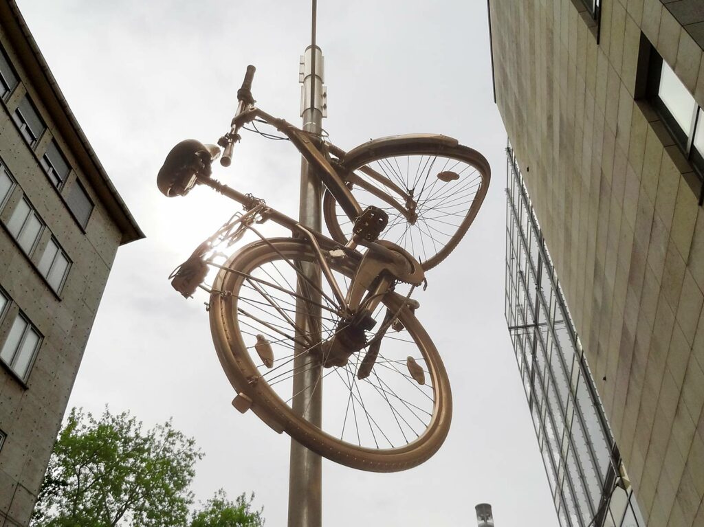 Goldenes Fahrrad hochkant befestigt an Wegweiser-Mast in Frankfurt