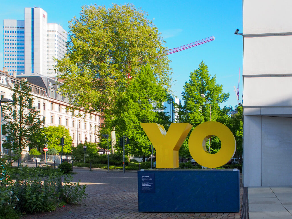 Gelbe Buchstaben auf blauem Podest – OY / YO von Deborah Kass vor dem Jüdischen Museum Frankfurt