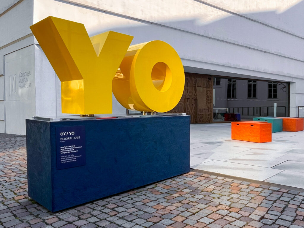 Gelbe Buchstaben auf blauem Podest – OY / YO von Deborah Kass vor dem Jüdischen Museum Frankfurt