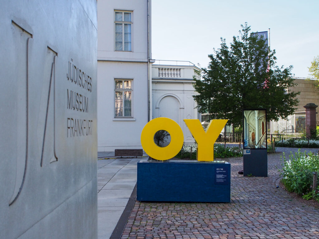 Gelbe Buchstaben auf blauem Podest – OY / YO von Deborah Kass vor dem Jüdischen Museum Frankfurt