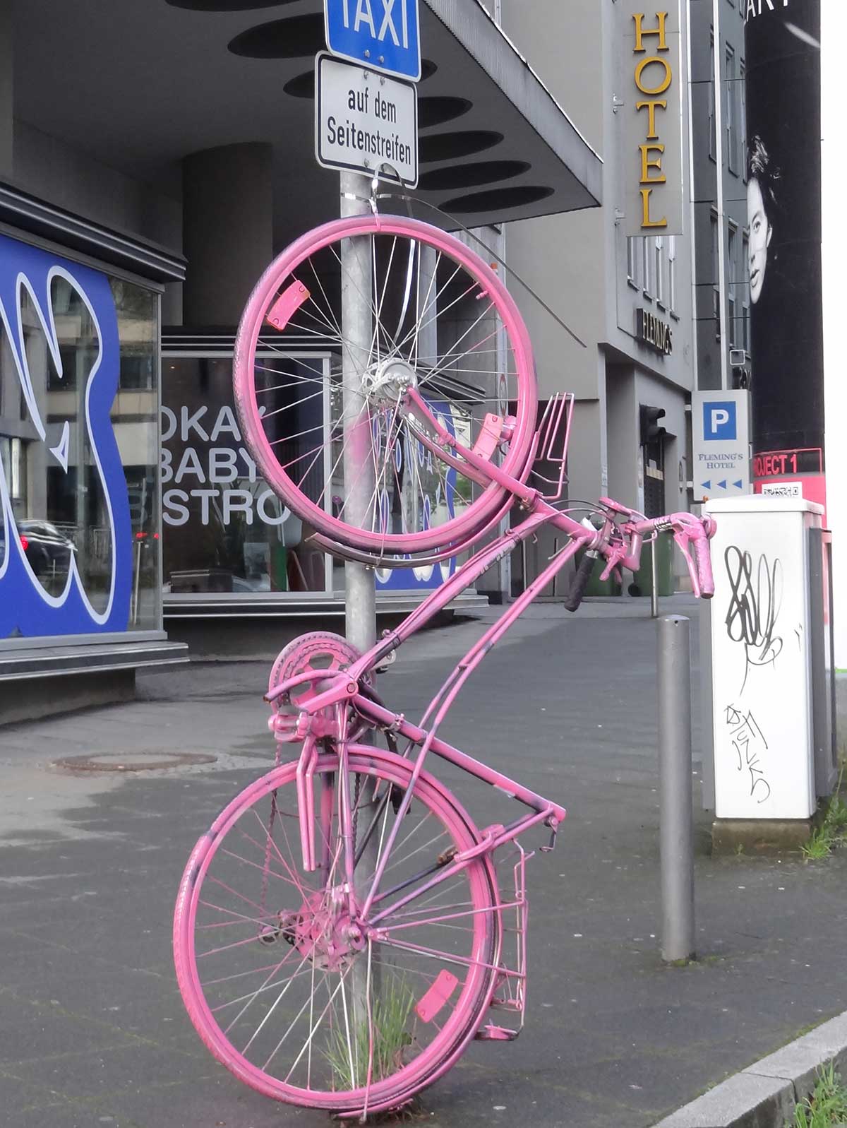 Pink farbenes Fahrrad hochkant befestigt an Verkehrsschild-Rohrpfosten in Frankfurt