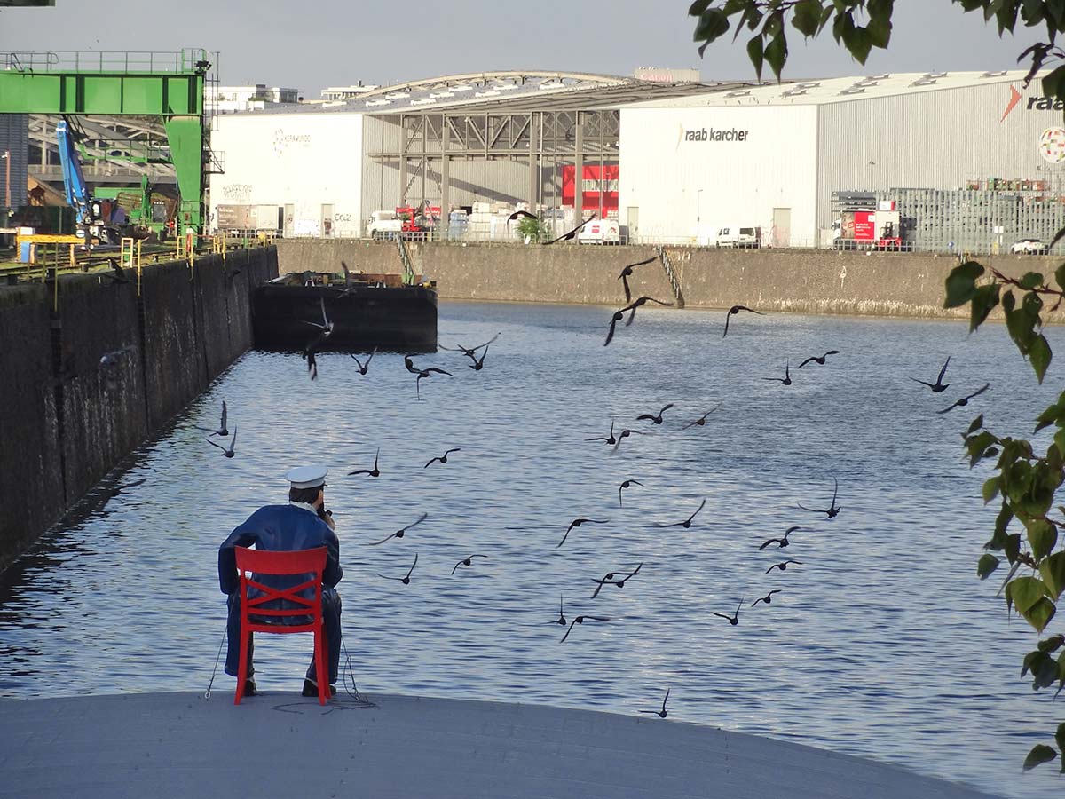 Seemann mit Pfeife auf rotem Stuhl am Hafenbecken im Osthafen Frankfurt