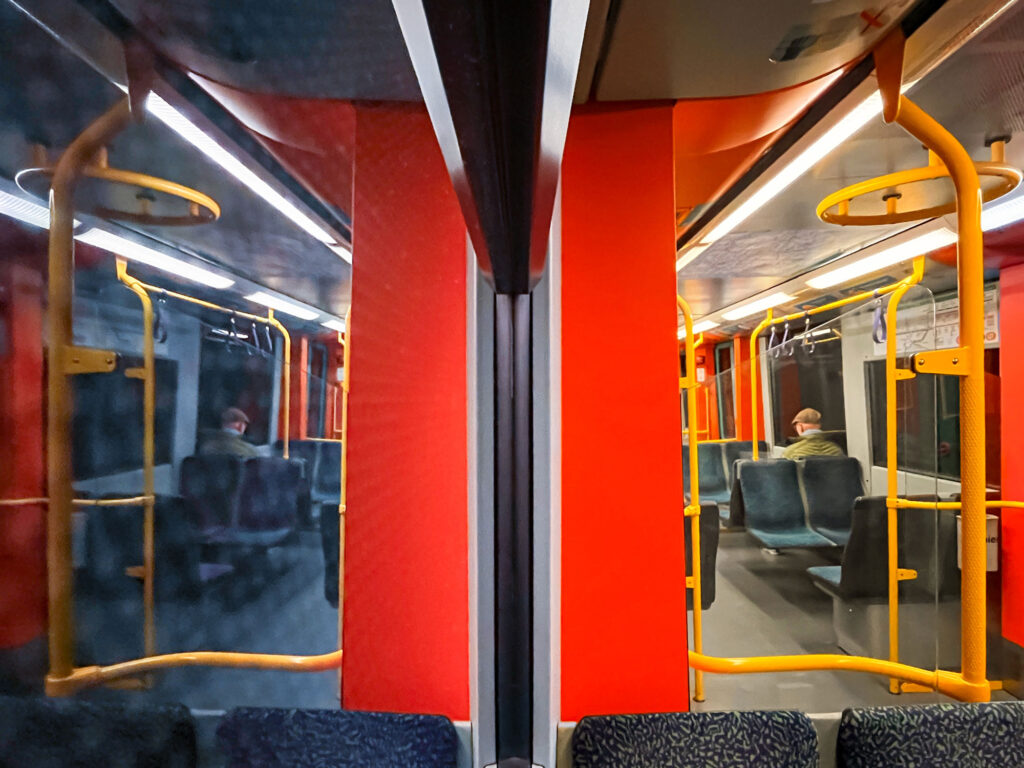 In einer U-Bahn in Frankfurt sitzend. Die eine Hälfte des Fotos zeigt das Innere des Waggons, die andere Hälfte dessen Spiegelung an der Fensterscheibe.