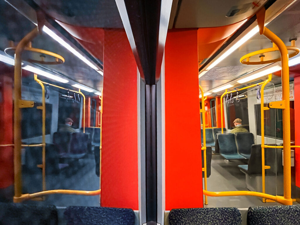 In einer U-Bahn in Frankfurt sitzend. Die eine Hälfte des Fotos zeigt das Innere des Waggons, die andere Hälfte dessen Spiegelung an der Fensterscheibe.